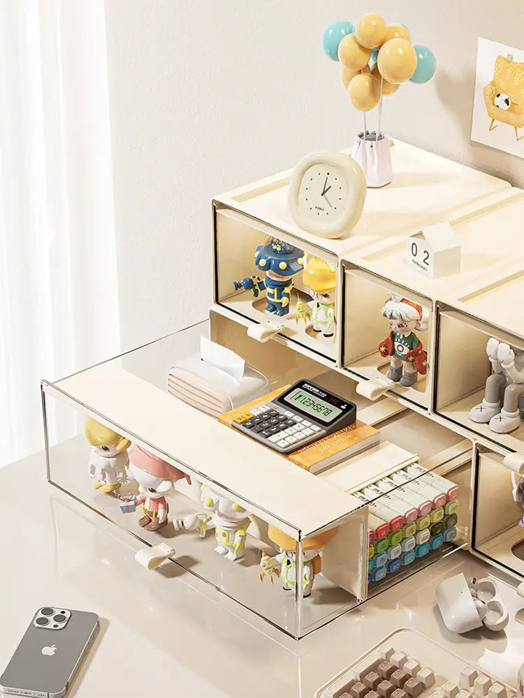 Beige and transparent acrylic desktop organizer and collectible display case with pull-out compartments holding figurines, a calculator, pens, and other small items.