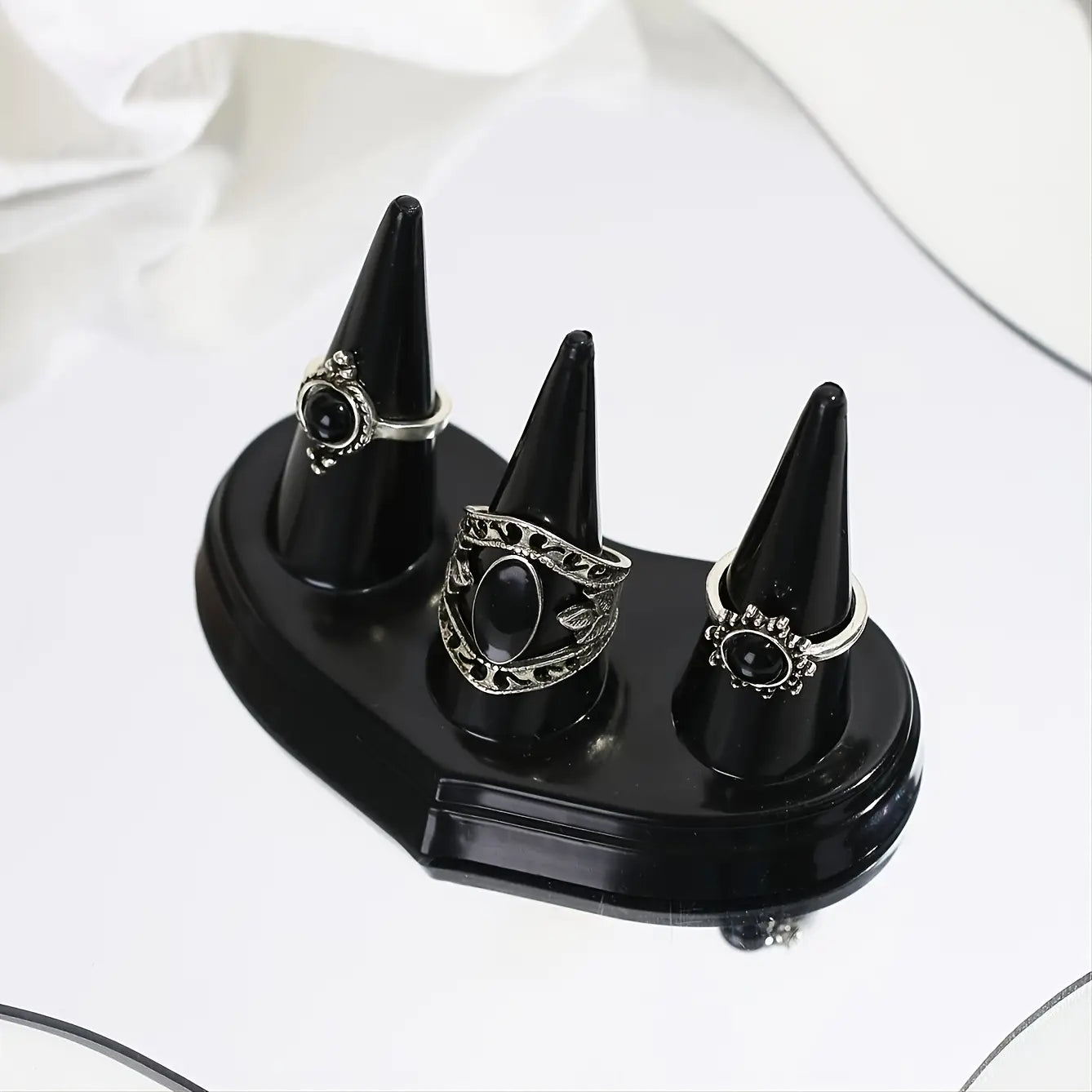Support d’exposition en plastique noir conique pour bagues, avec une finition brillante, tenant trois bagues argentées ornées de pierres ovales noires.