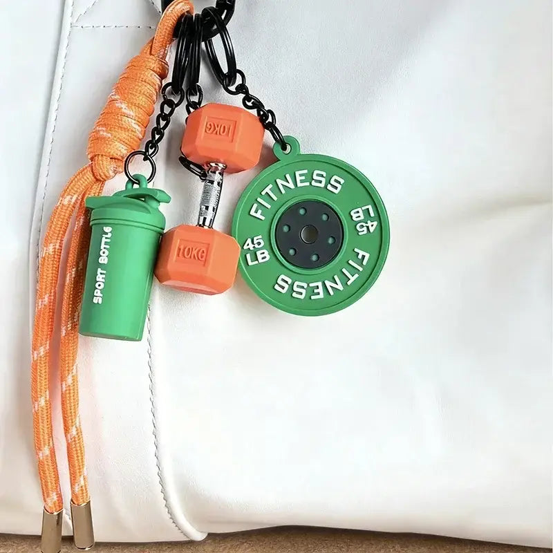 Orange and green silicone fitness keychain with dumbbell weight plate and shaker bottle charms designed as a colorful gym bag charm accessory.
