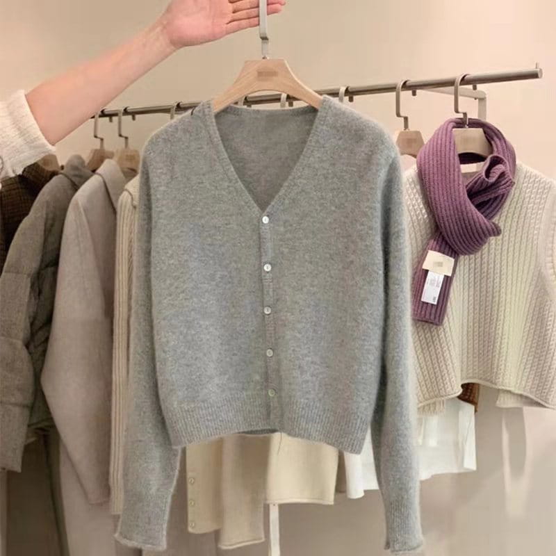 Un pull cardigan en laine mérinos gris chiné doux à encolure en V, avec fermeture boutonnée sur le devant et manches longues.