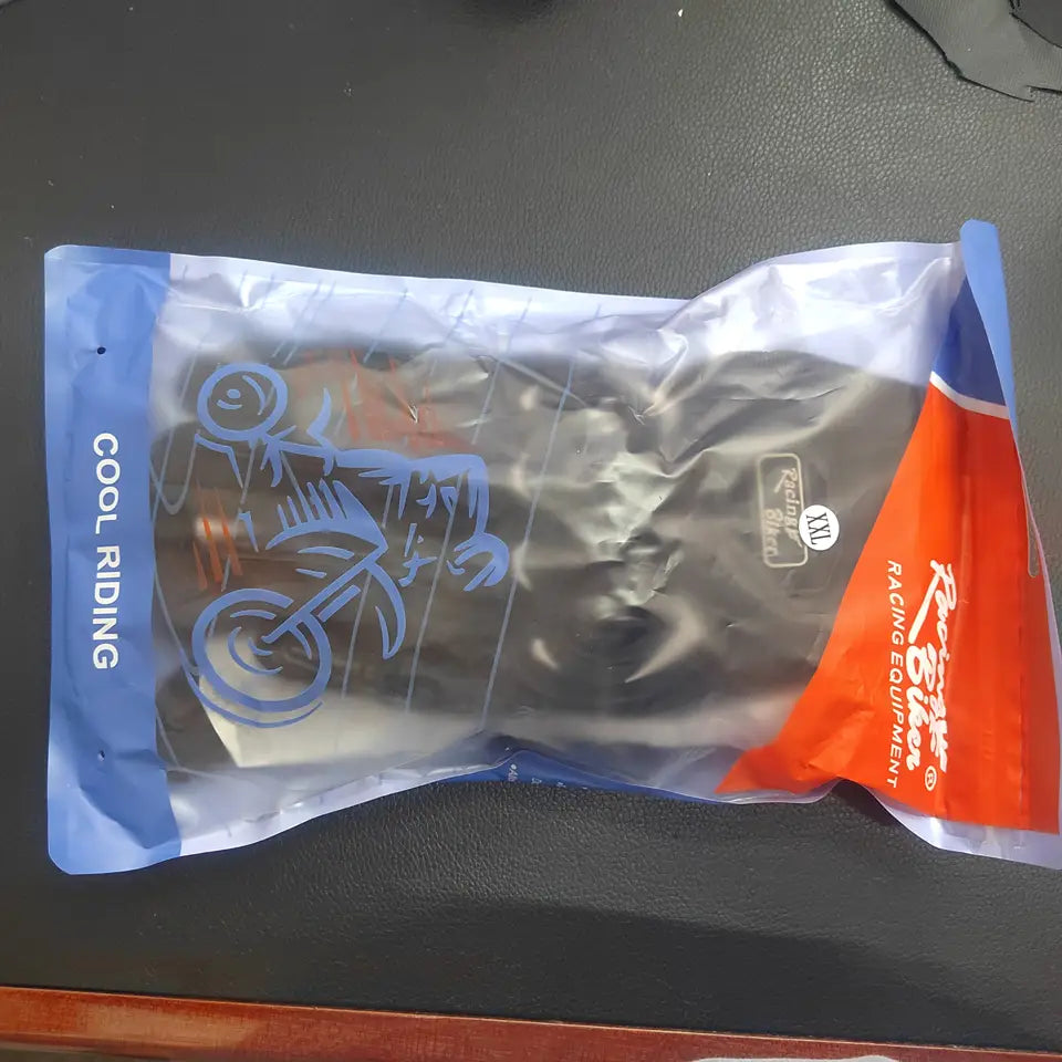 Black motorcycle racing gloves made of breathable protective material displayed in clear plastic packaging with blue and orange branding.