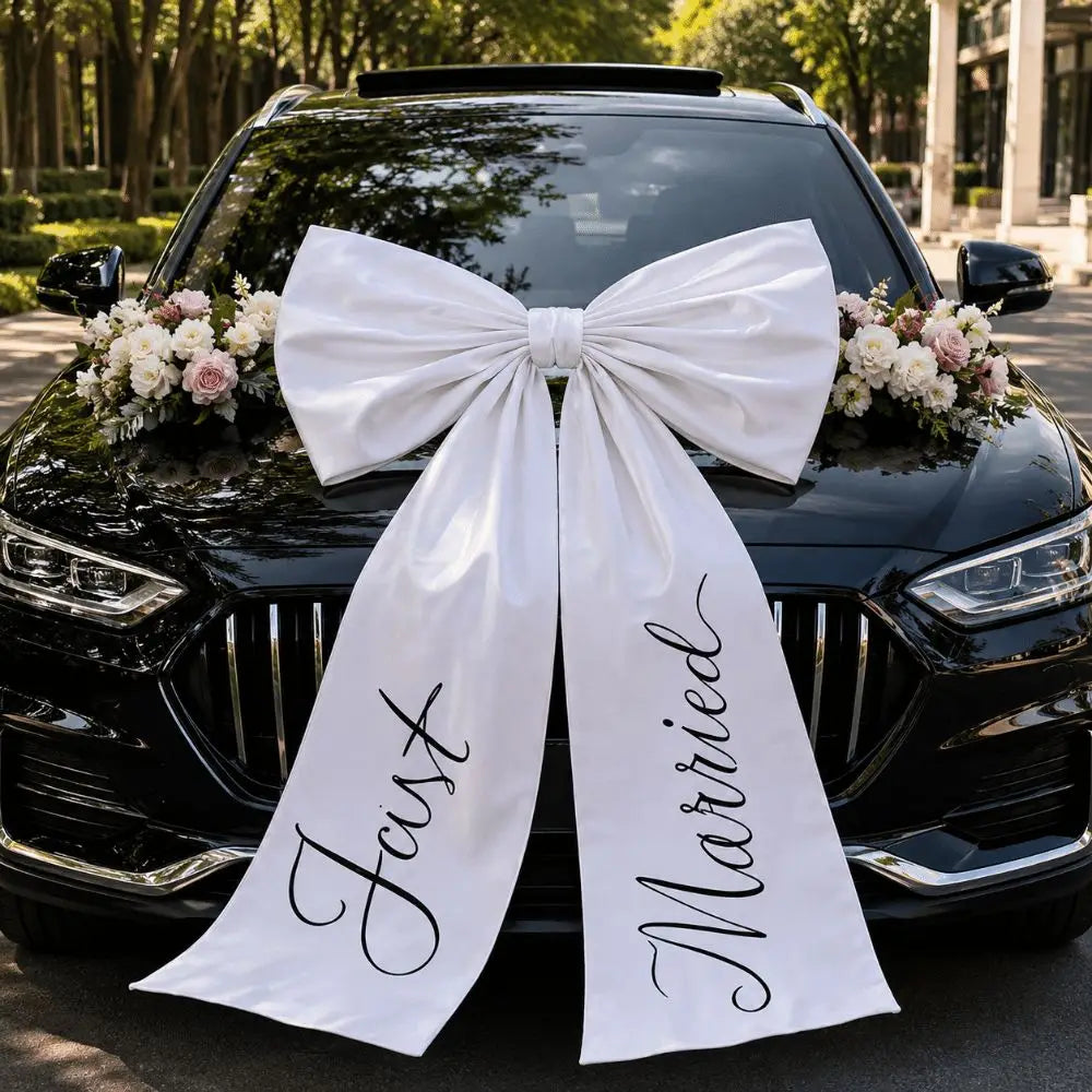 Un gran moño para coche de bodas de satén blanco con «just married» en cursiva negra sobre el capó de un automóvil.