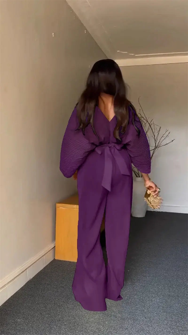 a flowing deep purple satin wrap-style jumpsuit with a v-neckline wide sleeves and a waist tie, part of a purple satin two piece set with wide leg pants
