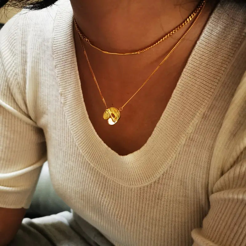 Collier pendentif à superposition géométrique doré pour femmes, présentant un collier en or avec un petit pendentif rond gravé d’un motif et une pierre d’accent blanche.