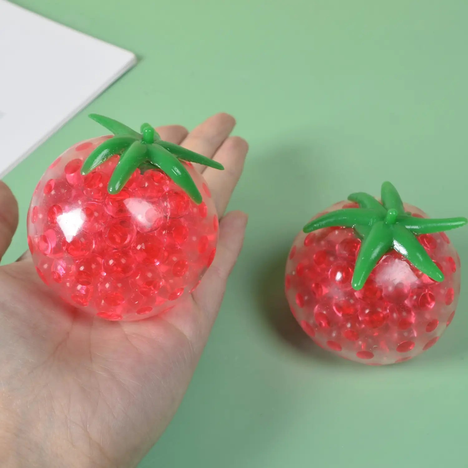 Red tomato-shaped squishy stress relief toy featuring a green plastic stem and translucent gel beads inside for squeeze ball use.