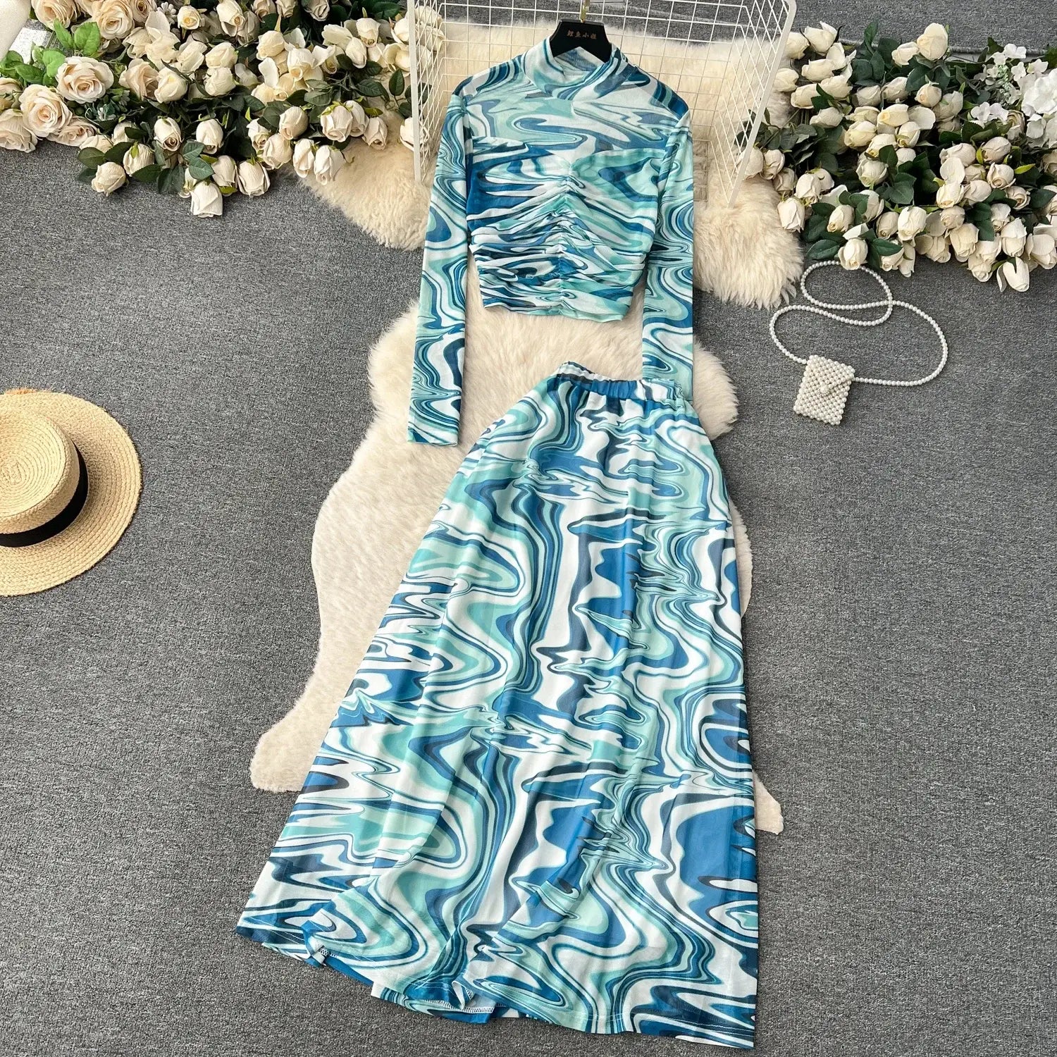 a two-piece mesh skirt set featuring a long-sleeved high-neck top and a flowing maxi skirt with an abstract blue and white marbled pattern and an elastic closure type