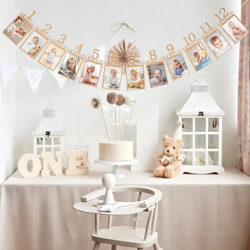 a delicate gold-colored photo banner made of durable material featuring numbered frames for baby milestones hanging above a white cake and decorative lanterns for first birthday celebrations