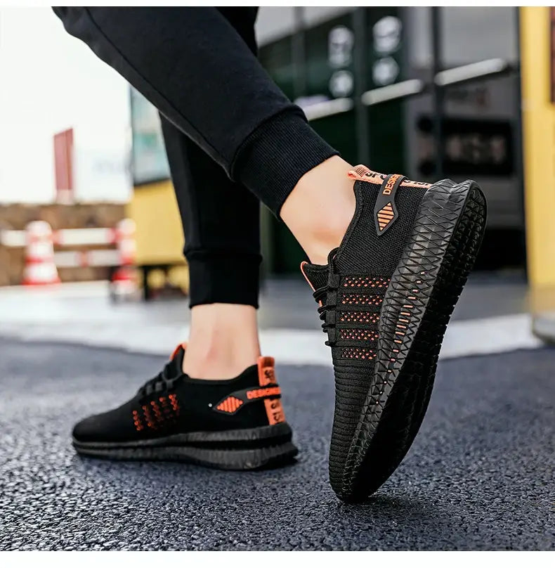 Herren-Atmungsaktive legere Strick-Sneaker in Schwarz und Orange mit strukturiertem Mesh-Obermaterial, geometrisch gemusterter Gummisohle und markierter Fersenlasche, von der Rückseite dargestellt