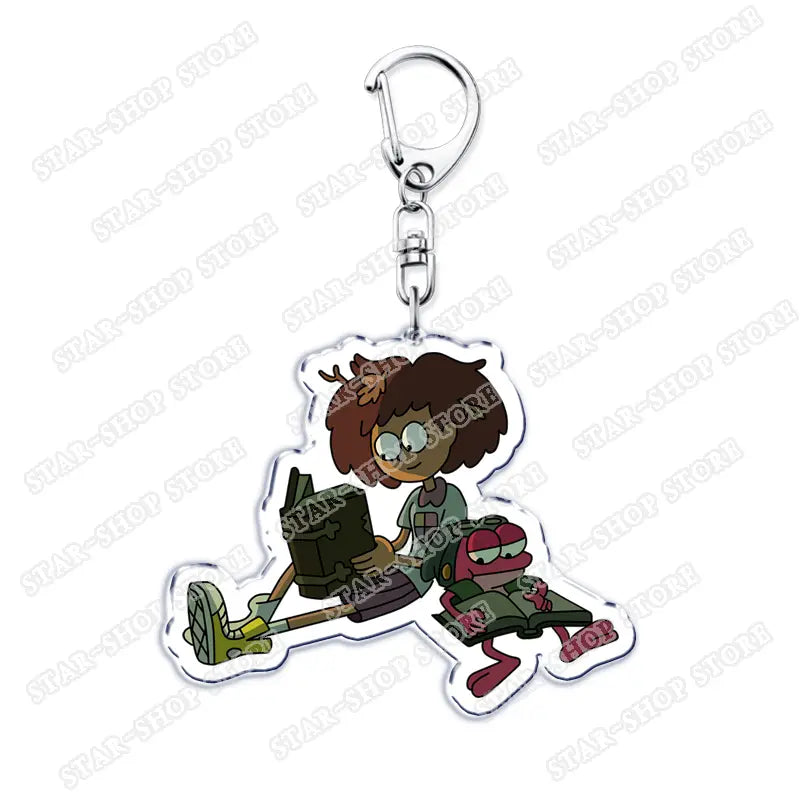 Clear acrylic Amphibia anime keychain featuring a cartoon character with brown hair and glasses sitting cross-legged reading a book alongside a small pink frog companion.