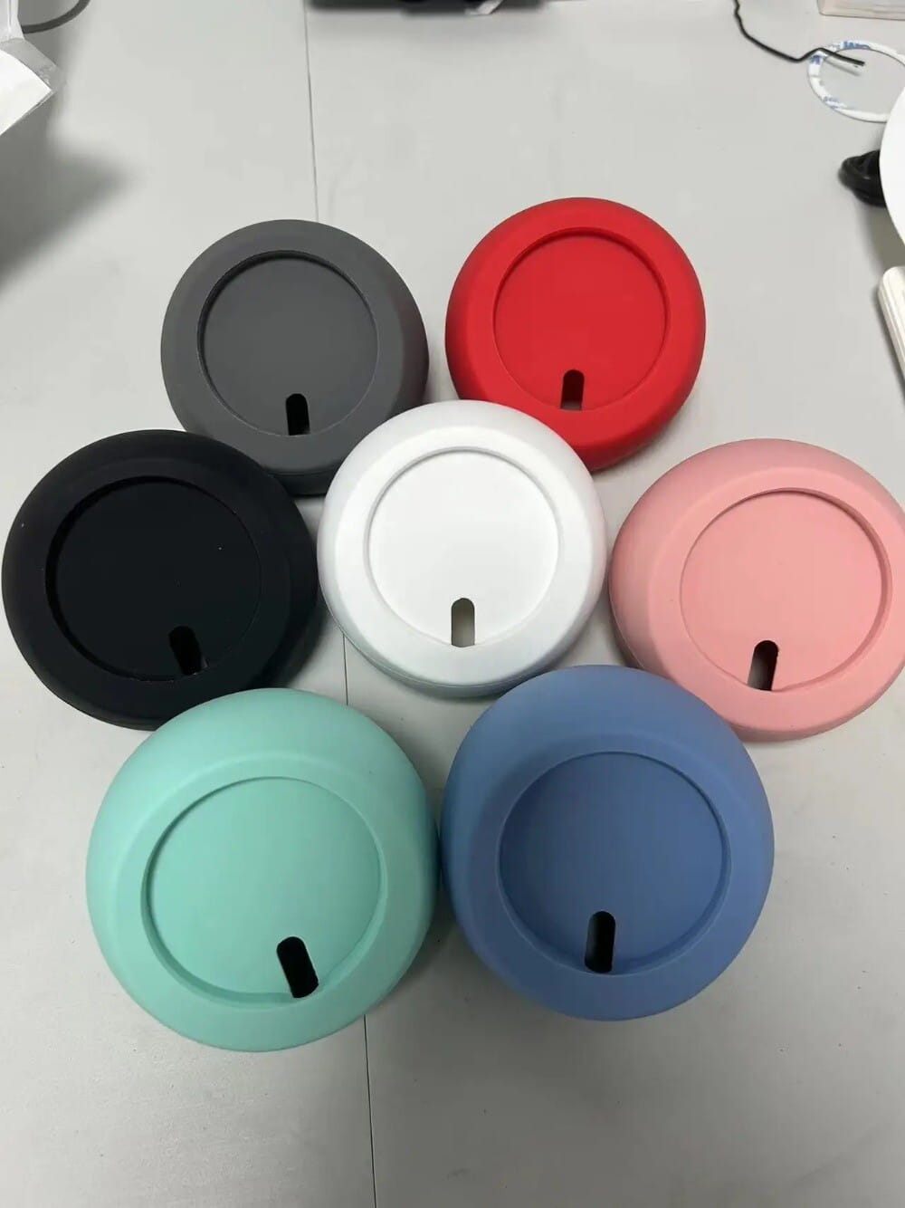 seis tapas de silicona para tazas de café de colores surtidos, incluidos negro, blanco, rojo, rosa, azul y verde azulado, mostradas con un soporte magnético inalámbrico de carga para teléfono para iPhone