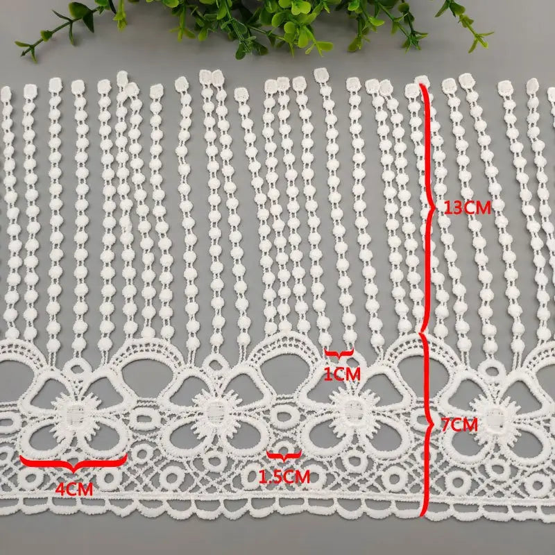 Tissu à bordure de dentelle à perles blanches, présentant de délicats motifs floraux blancs et un détail de perles complexe.