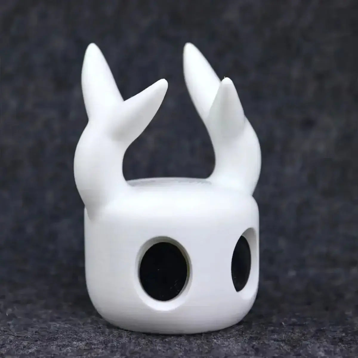 white ceramic hollow knight game controller stand for ps5 featuring two pointed antler-like horns and black circular eye sockets