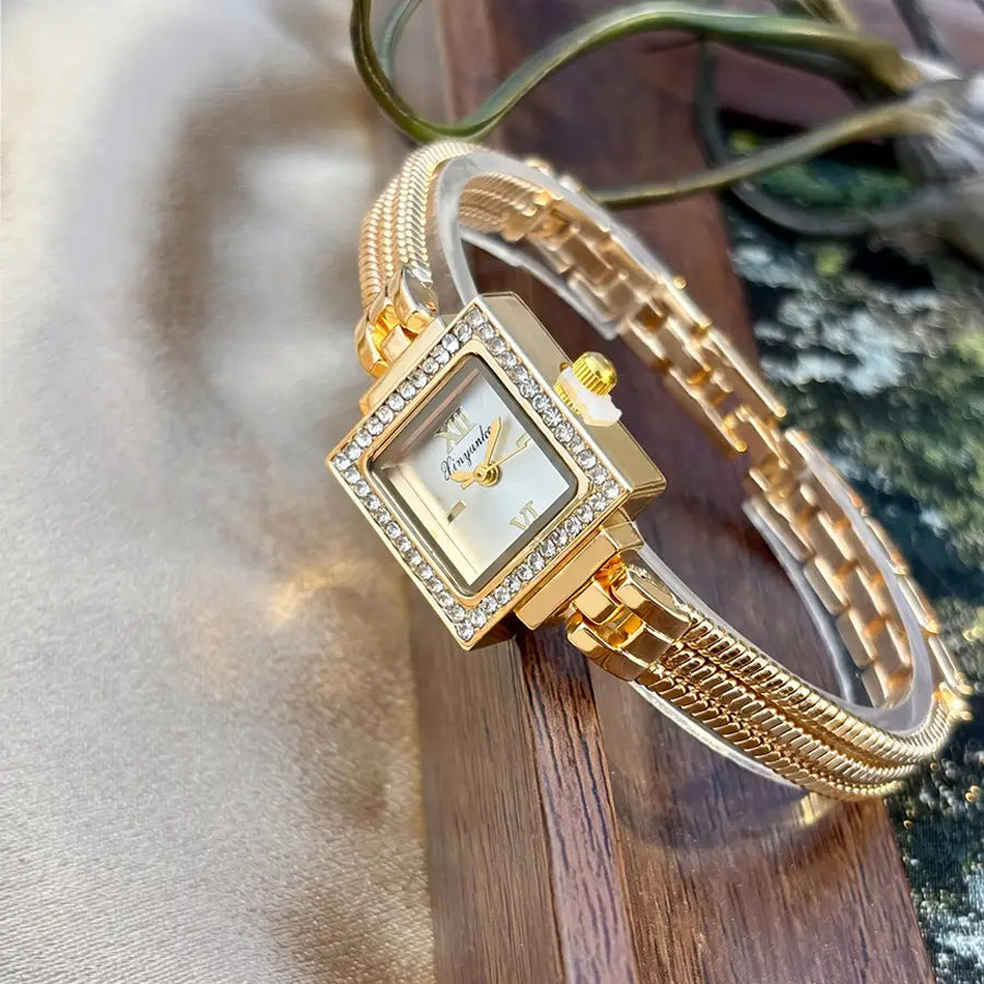 Gold diamond square watch with a gold-toned diamond-encrusted bezel, cream-colored dial with roman numeral markers, and an ornate braided metal fringe strap.