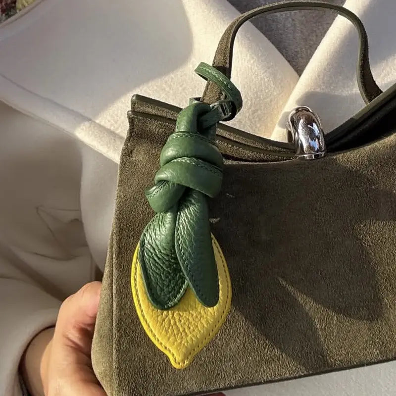 Un charm pour sac à main en forme de citron, en cuir vert et jaune, avec un dessus noué, conçu comme ornement de sac à main en cuir végétal.