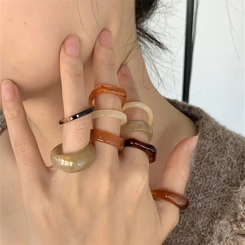 a collection of translucent amber-toned and black resin stackable rings with smooth rounded edges worn on multiple fingers in a bohemian retro style design using resin material