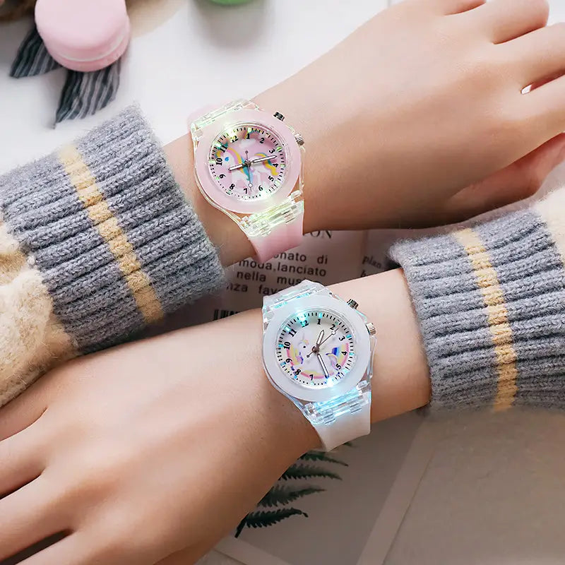 two translucent glowing led wristwatches with colorful unicorn-themed faces and pink and white silicone straps worn on gray sweaters for kids unicorn led light up silicone digital watch