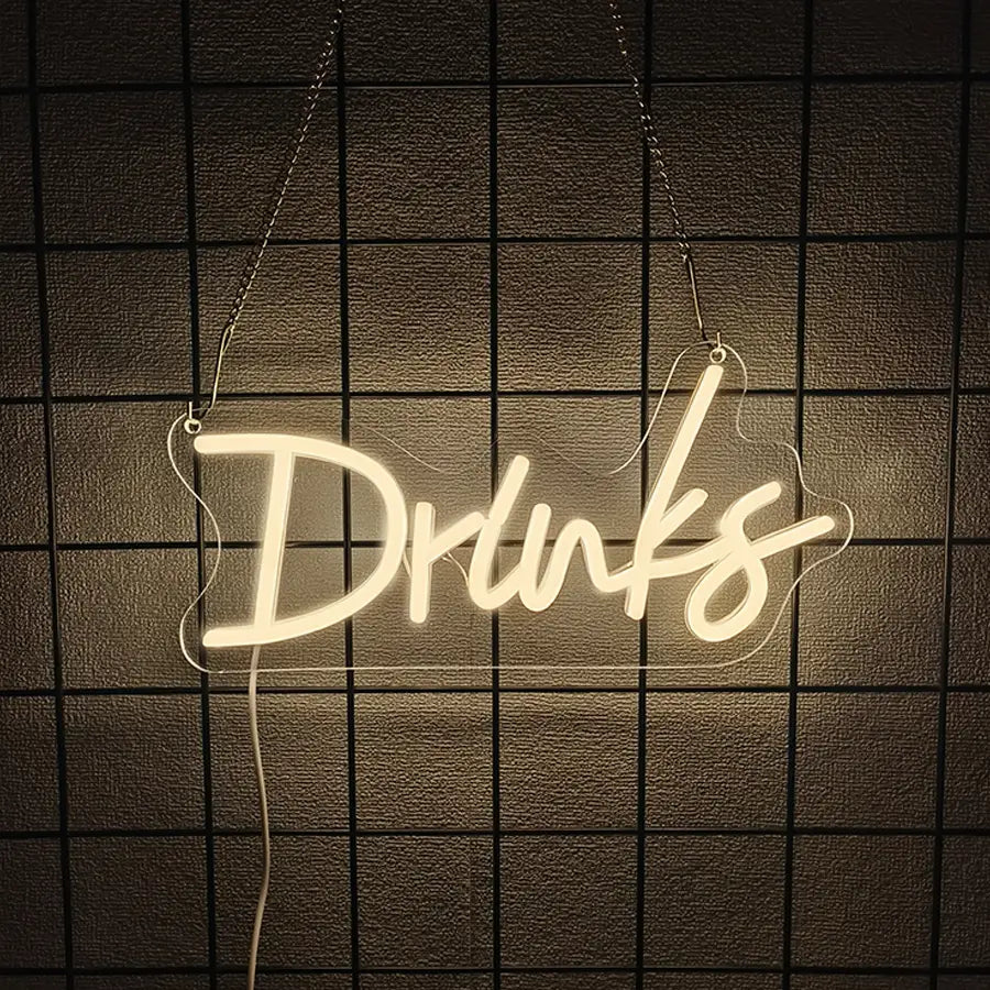 une enseigne au néon blanc lumineux avec le mot « drinks » dans une écriture cursive suspendue par des chaînes, en décoration murale à LED contre un mur carrelé sombre, destinée à un cadre de boisson ou de bar