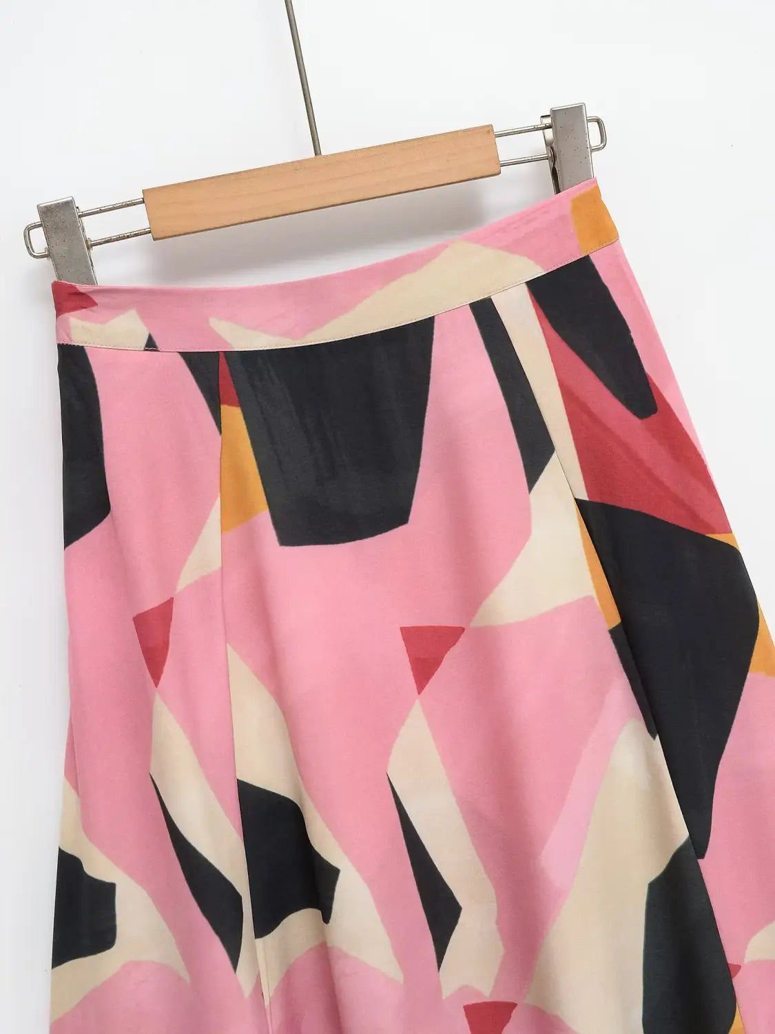 Ein lebhafter rosa-schwarz-cremiger geometrischer Satin-Midirock mit einem abstrakten Muster, das an einem Holzkleiderbügel hängt.