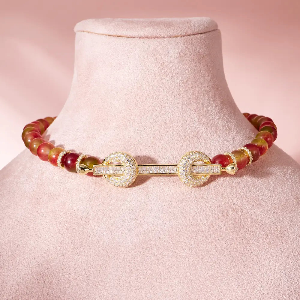 Un lujoso collar tipo choker con cuentas de tono dorado, con un broche central de circonita cúbica engastado tipo pave y cuentas vibrantes de color rojo y ámbar.