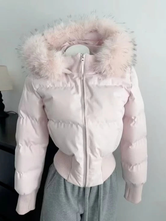Ein Damen-Winter-Steppmantel in sanftem Rosa mit einer flauschigen Kunstfell-Kapuze in hellem Farbton und gerippten Bündchen, konzipiert für kaltes Wetter.