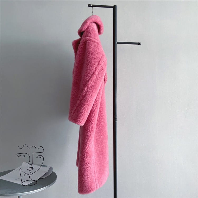 Abrigo exterior tipo osito de peluche largo para mujer de lana en color rosa vibrante, esponjoso, con contorno de pecho adecuado para abrigo de invierno, colgado ordenadamente en una estructura metálica negra.