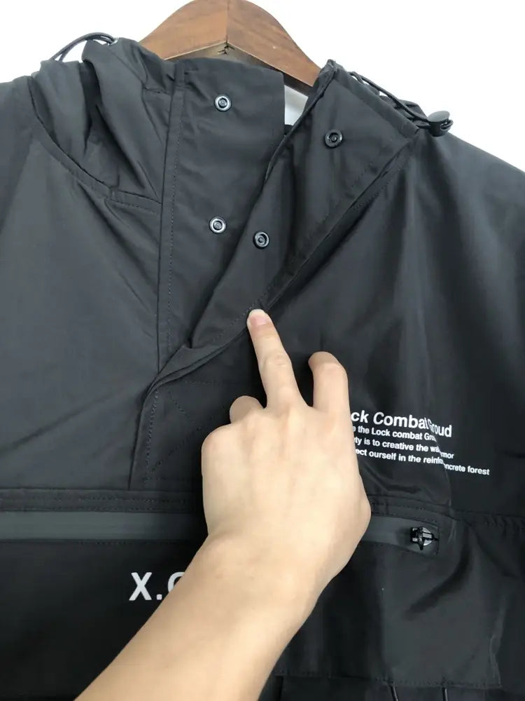 Veste imperméable à capuche tactique techwear noire, avec capuche, fermeture zippée avant et marquage en texte blanc sur la poitrine.