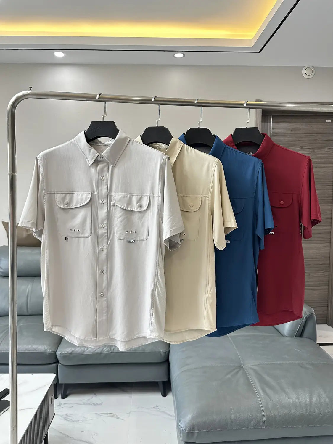 Eine Kollektion von Herren-Stretch-Outdoorhemden mit kurzen Ärmeln und Knopfverschluss in Creme, Beige, Blau und Rot mit schnelltrocknendem Stoff und zwei Brusttaschen mit subtilen Ziernähte-Details.