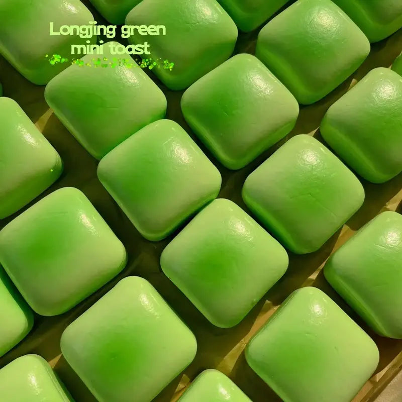 Bright green square-shaped longjing green mini toast pastries with a smooth glossy surface in a slow rising squishy mini toast fidget toy.