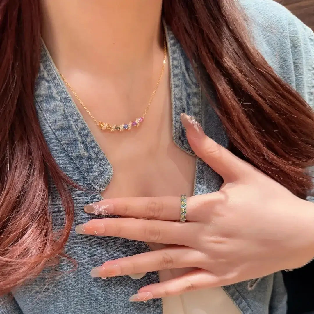 Un collier délicat en chaîne or surmonté d'argent, orné d'une rangée de pierres précieuses multiples facettées et colorées dans un design de pendentif géométrique.