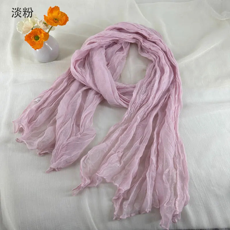 Écharpe en coton et lin plissé rose pâle délicat, avec une texture froissée douce et des bords effilochés.