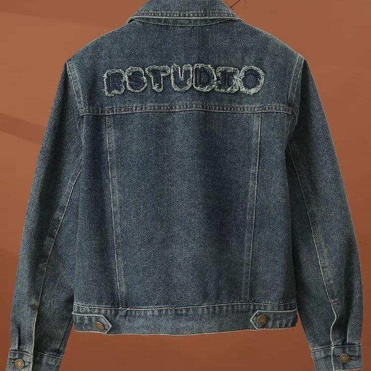 The back side of a dark blue denim embroidered star denim jacket features rstudio embroidered in textured slightly frayed stitching.