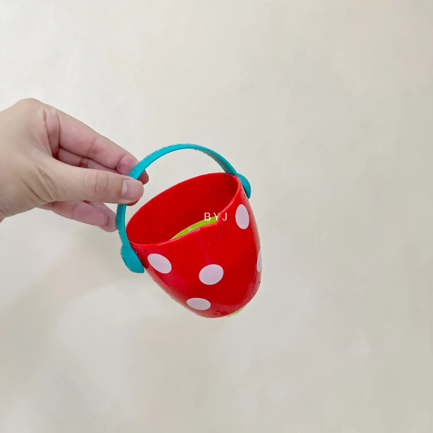 Ein roter Kunststoff-Badewannen-Eimer für Babys mit weißen Punkten und einem tealfarbenen Griff, entworfen als Wassersprühspielzeug-Set.