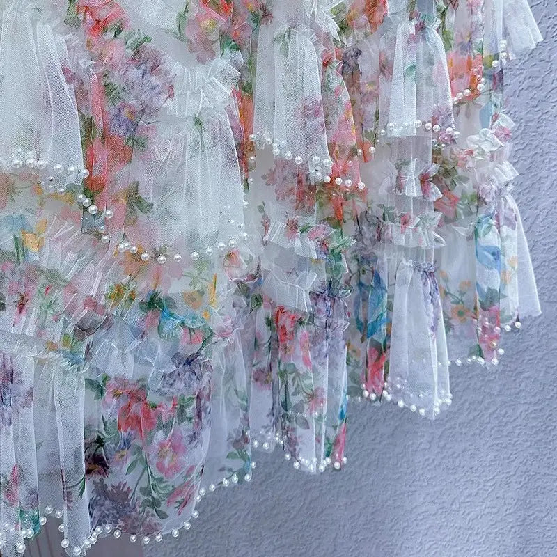 Una falda de tul floral fairycore delicada en tonos pastel suaves, con tejido translúcido fruncido de múltiples capas y bordes rematados con perlas.