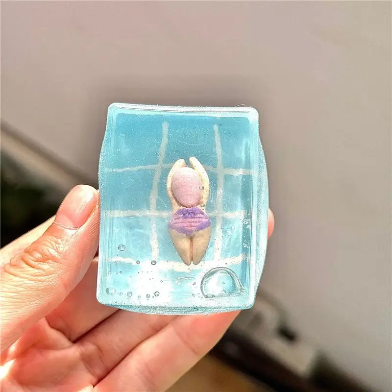 un cube sphérique translucide bleu à faible rebond, visqueux et lent, présentant une mini figurine de nageur dans un maillot violet, enfermé dans un design de piscine glacée