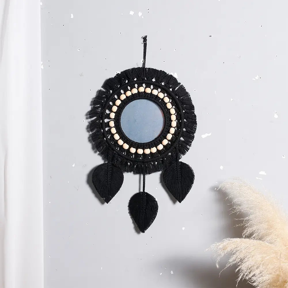 Black macrame round wall mirror featuring a central mirror, cream-colored beads around the rim, and three black leaf-shaped tassels, serving as a decorative mirror with boho style.
