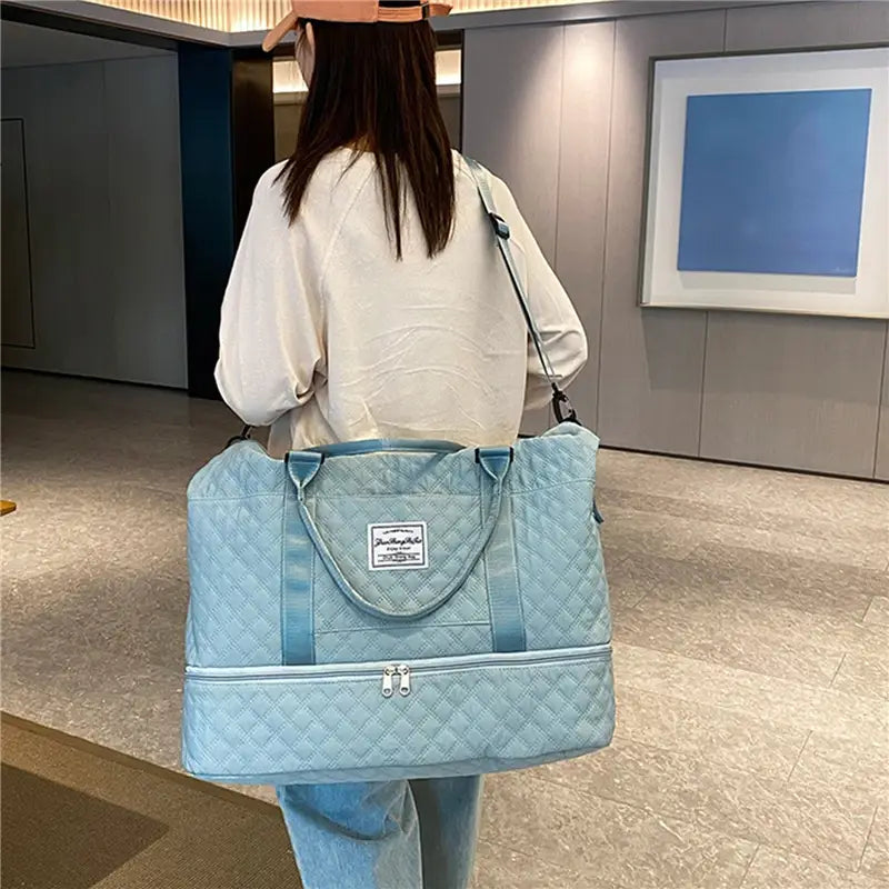 Bolsa de viaje tipo duffel acolchada azul claro con asas superiores y compartimento frontal con cierre, diseñada como un tote weekender grande.