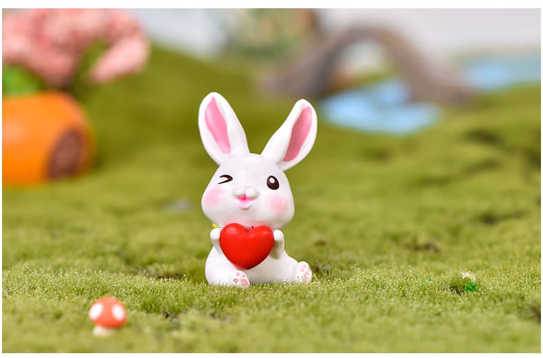 Une figurine miniature en résine céramique blanche de lapin, avec des oreilles internes et des joues roses, tenant un cœur rouge pour la décoration d’un jardin féerique.