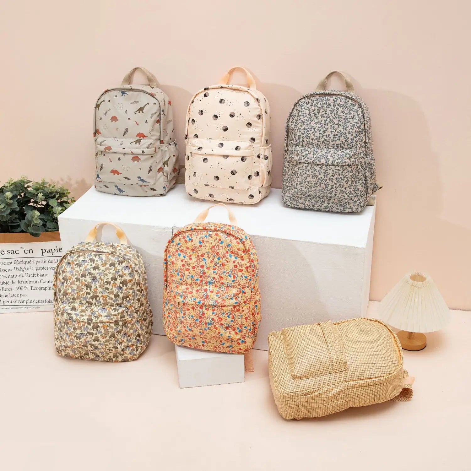 Un sac à dos beige à motifs floraux pour enfants, en texture tissée, avec des anses assorties, conçu comme un sac d’école pastel.