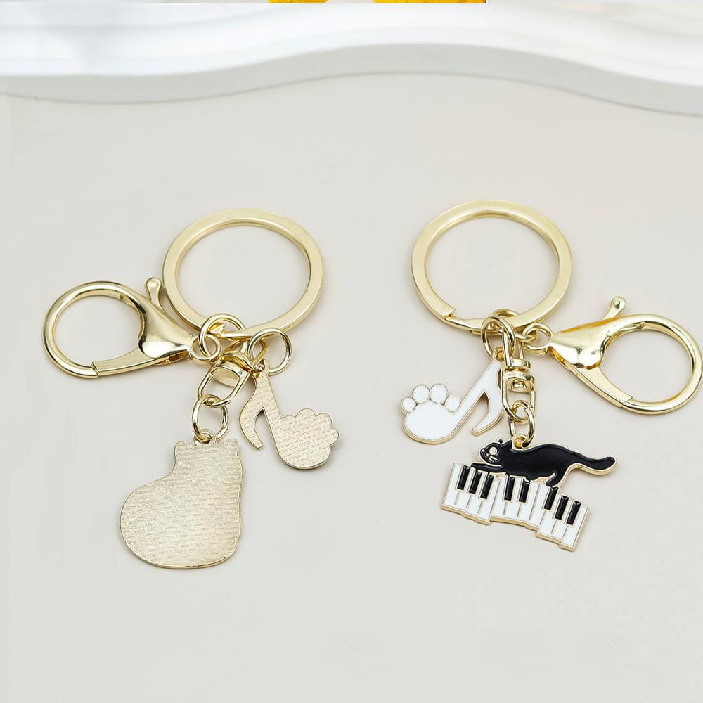 Gold-toned keychains featuring musical-themed charms including a piano-shaped pendant and an enamel black cat leaping over keys for music lovers gift