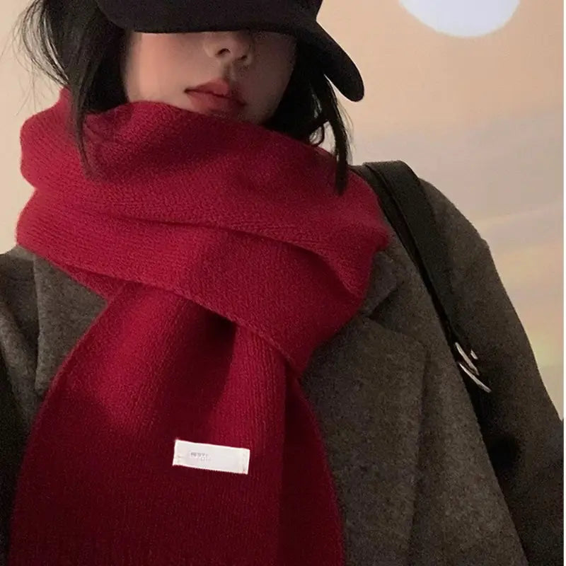 Una bufanda de invierno tejida en rojo, acogedora y vibrante, para hombres y mujeres, con una textura suave y una pequeña etiqueta blanca cosida cerca de la parte inferior.