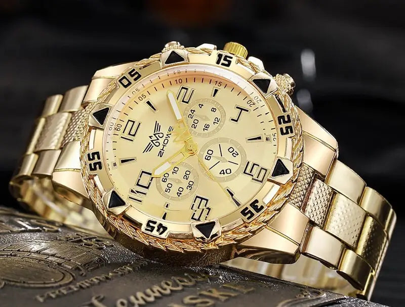 Montre à quartz à chronographe en acier inoxydable Tvk avec un boîtier couleur dorée, un bracelet métallique texturé, et un cadran couleur crème comprenant des chiffres noirs, des marqueurs triangulaires et trois sous-cadrans.