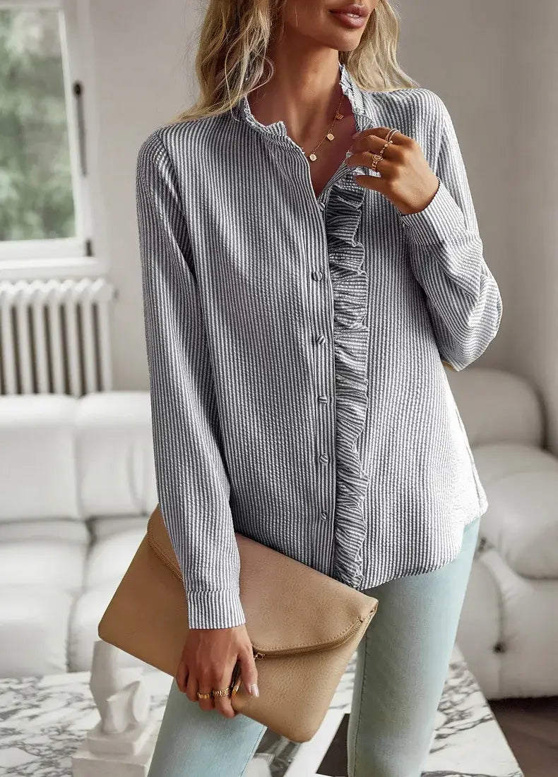 Una mujer lleva una blusa blanca de textura con manga larga, con rayas verticales grises y blancas y detalles con volantes a lo largo del canesú delantero.