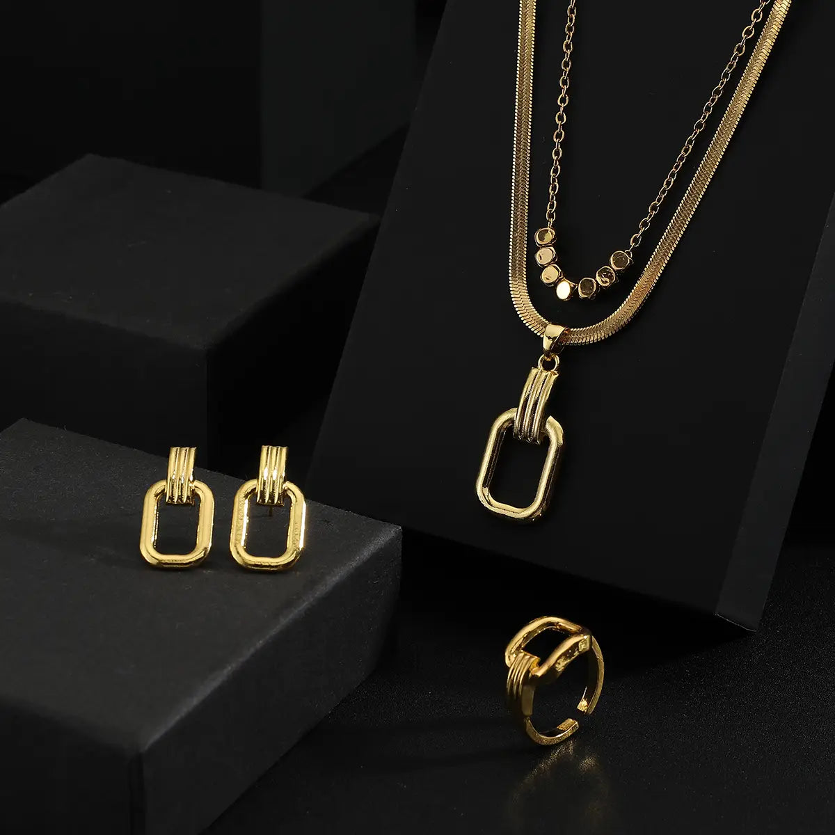 Juego de joyería de acero inoxidable color dorado para mujeres, con un collar de eslabones rectangulares con un dije a juego y detalle de cadena.