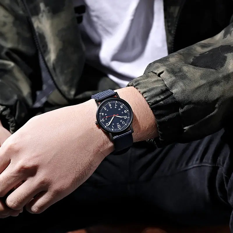 Schwarze analoge Militär-Quarzuhr mit strukturiertem dunkelblauem Stoffarmband und minimalistischen Zifferblatt mit weißen Ziffern sowie rotem Sekundenzeiger.
