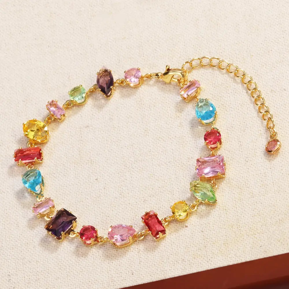 A vibrant gold-toned bracelet adorned with colorful faceted zircon crystals in shades of pink blue yellow green and purple in a gold plated design.