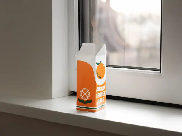 Un vase en céramique vibrant orange et blanc, conçu comme une brique de jus d’orange, avec une touche de feuille verte et un style rétro classique.