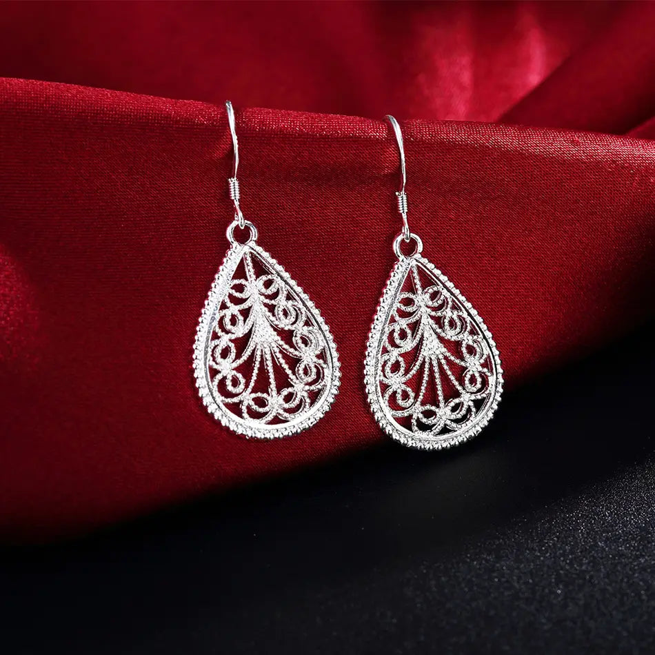 Boucles d’oreilles en forme de goutte en argent sterling présentant un motif filigrané complexe et un bord rehaussé de petites perles, dans un ensemble de bijoux.