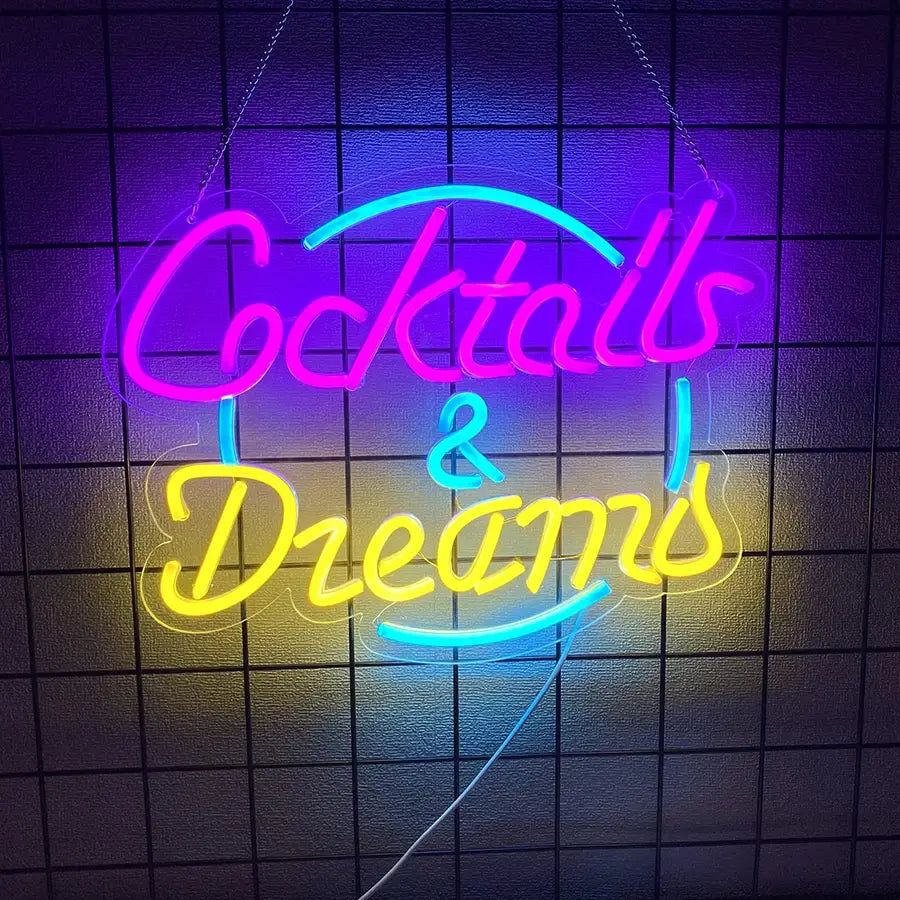 Une enseigne néon vibrante affichant les mots « cocktails and dreams » en tubes lumineux rose, jaune et bleu, conçue pour un usage décoratif.