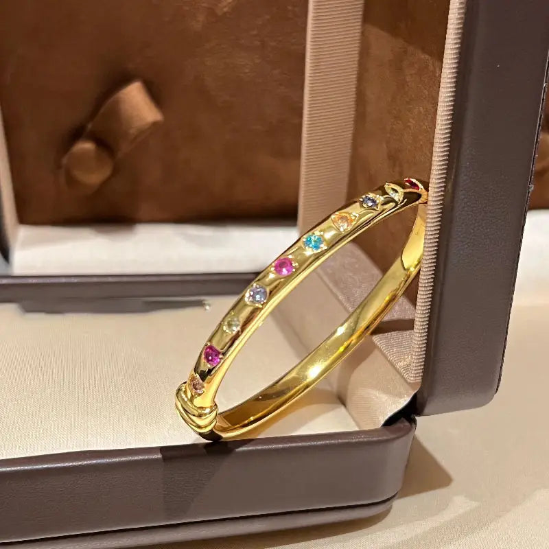 Ein lebhaftes Armreifarmband aus goldfarbenem Multigemsteinschmuck mit einer Reihe facettierter Edelsteine in Pink, Blau, Gelb und Klar.