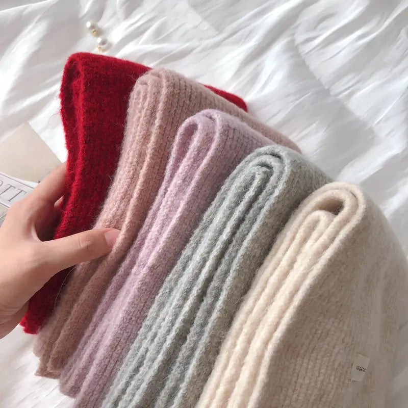 柔らかなリブ編みの女性用ニットカシミヤ冬用ストールの束を手に持った画像。赤、ピンク、ラベンダー、グレー、クリームを含むパステルカラーと鮮やかな色合い。